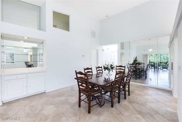 dining area featuring ceiling fan, light tile patterned floors, and a towering ceiling