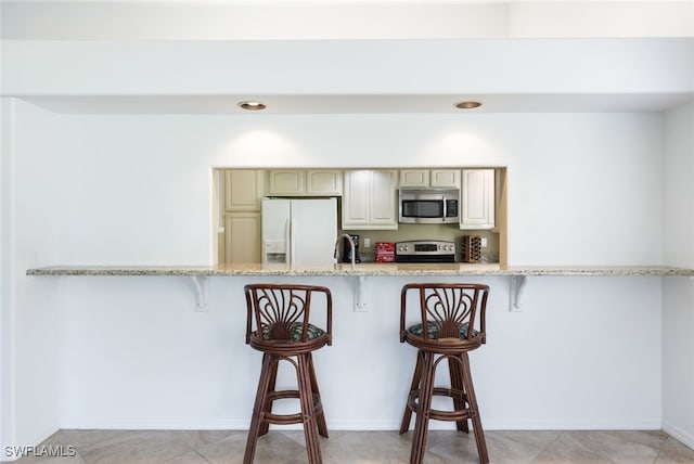 kitchen featuring white fridge with ice dispenser, light stone countertops, range, and a breakfast bar