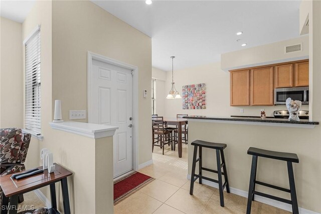 kitchen featuring kitchen peninsula, stainless steel appliances, light tile patterned flooring, and decorative light fixtures