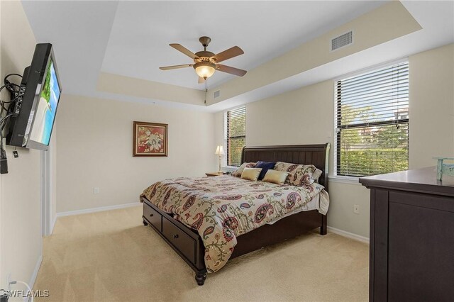 bedroom with a tray ceiling, light colored carpet, and ceiling fan