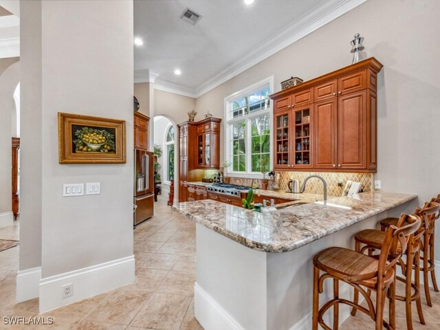 kitchen with kitchen peninsula, light stone countertops, appliances with stainless steel finishes, and a breakfast bar area