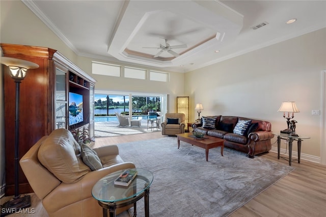 living room featuring ceiling fan, ornamental molding, a tray ceiling, and light wood-type flooring