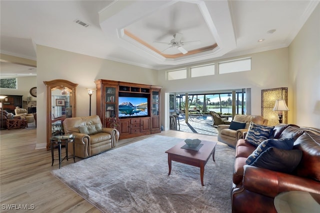 living room with crown molding, ceiling fan, a towering ceiling, a tray ceiling, and light hardwood / wood-style floors