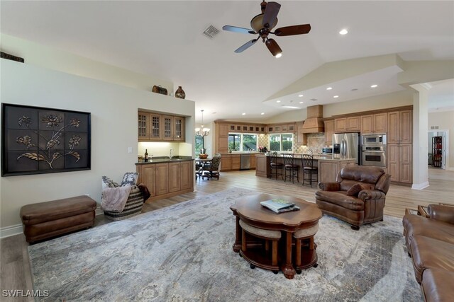 living room with ceiling fan with notable chandelier, lofted ceiling, sink, and light hardwood / wood-style flooring