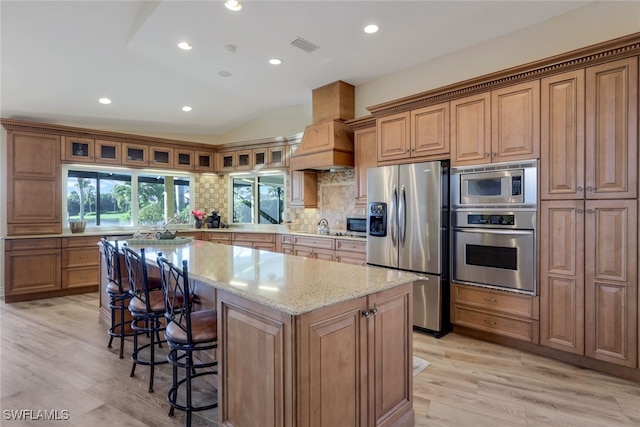 kitchen with custom exhaust hood, a kitchen island, stainless steel appliances, light stone countertops, and decorative backsplash