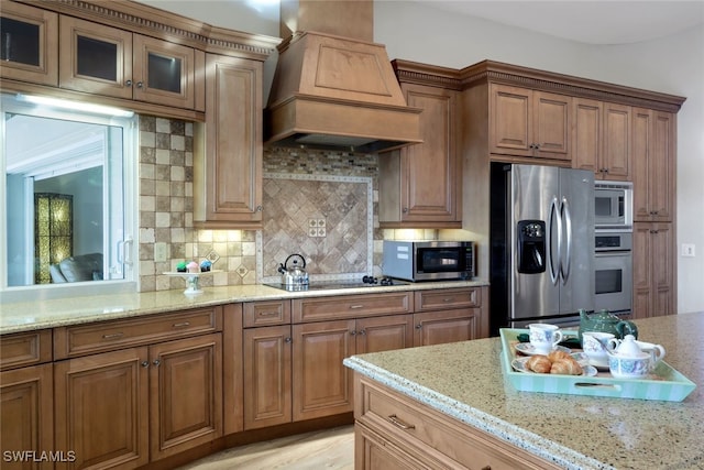 kitchen featuring light stone countertops, decorative backsplash, stainless steel appliances, and custom range hood