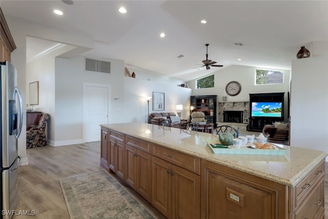 kitchen featuring stainless steel fridge with ice dispenser, vaulted ceiling, light stone countertops, and a kitchen island