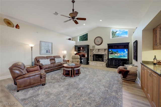 living room featuring ceiling fan, a stone fireplace, high vaulted ceiling, and light hardwood / wood-style floors