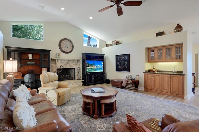 living room with ceiling fan, high vaulted ceiling, a fireplace, bar area, and light wood-type flooring