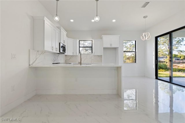 kitchen with tasteful backsplash, kitchen peninsula, white cabinets, and hanging light fixtures