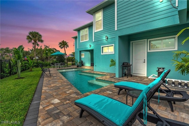 pool at dusk featuring a lawn, area for grilling, and a patio