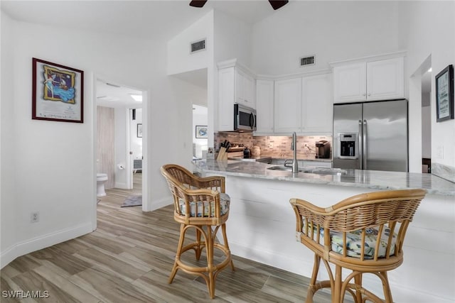 kitchen featuring stainless steel appliances, tasteful backsplash, light stone countertops, white cabinets, and kitchen peninsula