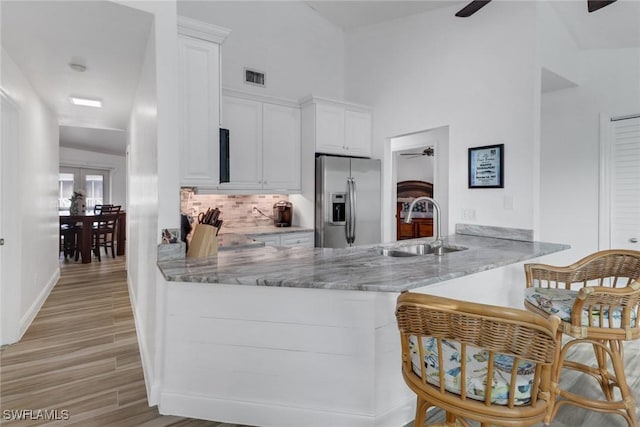 kitchen with ceiling fan, kitchen peninsula, white cabinets, and stainless steel refrigerator with ice dispenser