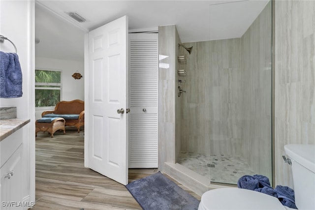 bathroom with hardwood / wood-style flooring, vanity, tiled shower, and toilet