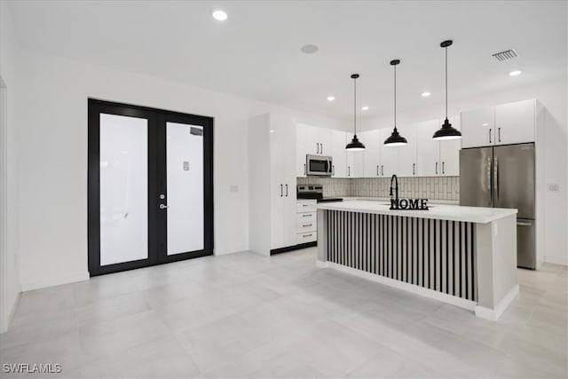 kitchen featuring an island with sink, hanging light fixtures, stainless steel appliances, decorative backsplash, and white cabinets