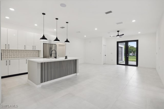 kitchen with stainless steel refrigerator, white cabinetry, decorative light fixtures, ceiling fan, and a center island with sink