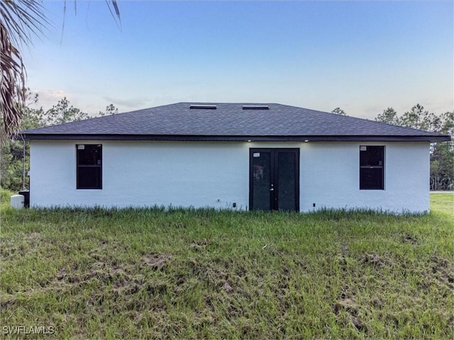 back of house featuring stucco siding, a lawn, and a shingled roof