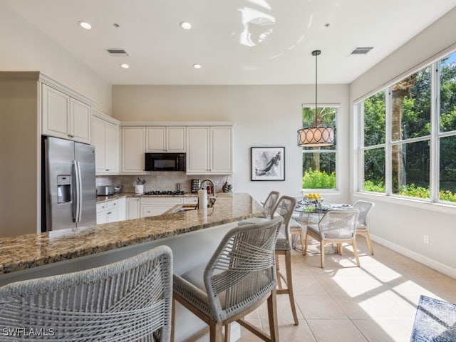 kitchen featuring white cabinets, hanging light fixtures, kitchen peninsula, stainless steel appliances, and light stone countertops