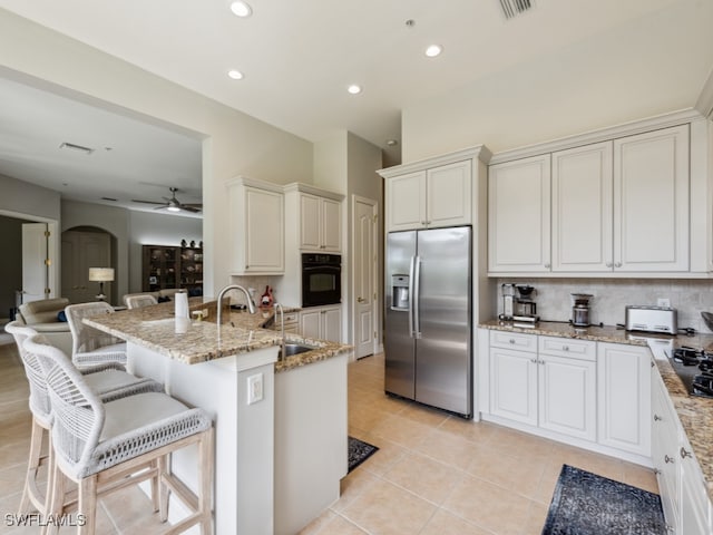 kitchen featuring light stone counters, decorative backsplash, black appliances, light tile patterned floors, and ceiling fan