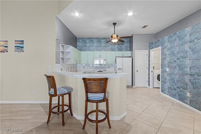 kitchen featuring ceiling fan, tasteful backsplash, kitchen peninsula, washer / clothes dryer, and white appliances