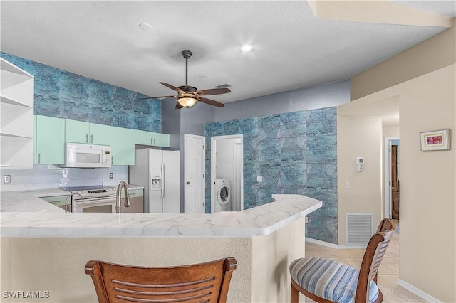 kitchen featuring white appliances, a kitchen breakfast bar, ceiling fan, washer / dryer, and kitchen peninsula