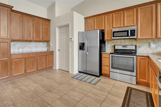 kitchen featuring backsplash, vaulted ceiling, light tile patterned floors, appliances with stainless steel finishes, and light stone counters