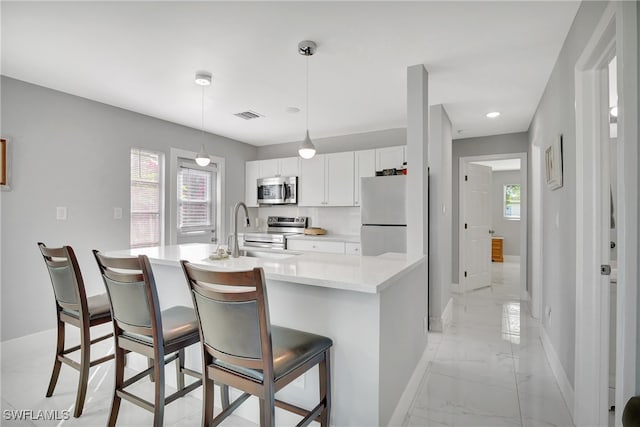 kitchen with white cabinetry, a kitchen breakfast bar, sink, hanging light fixtures, and appliances with stainless steel finishes