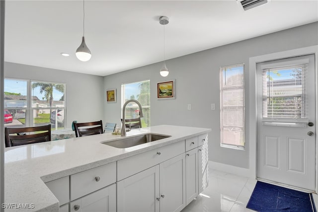 kitchen featuring light stone countertops, hanging light fixtures, white cabinetry, and sink