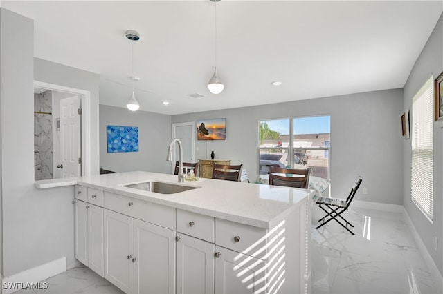 kitchen featuring pendant lighting, kitchen peninsula, sink, white cabinetry, and light stone counters