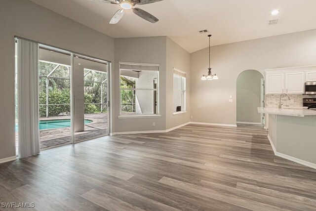 unfurnished living room with lofted ceiling, ceiling fan with notable chandelier, and wood-type flooring