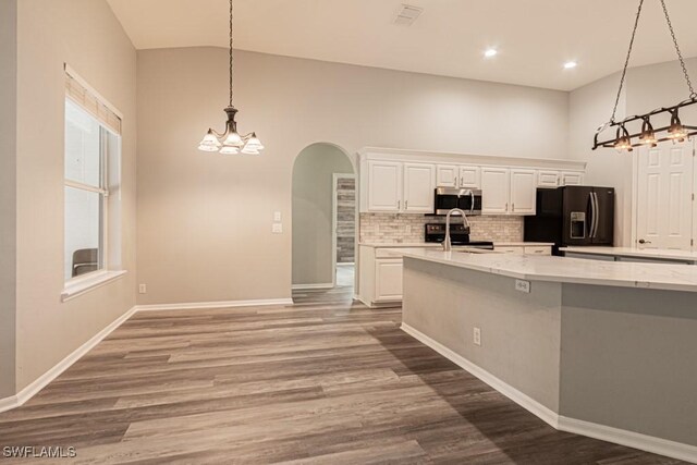 kitchen with black refrigerator with ice dispenser, pendant lighting, hardwood / wood-style flooring, light stone counters, and white cabinets