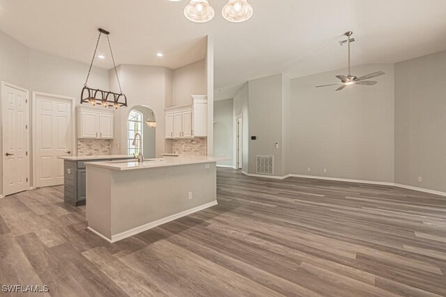 kitchen with dark wood-type flooring, ceiling fan with notable chandelier, hanging light fixtures, and a kitchen island with sink