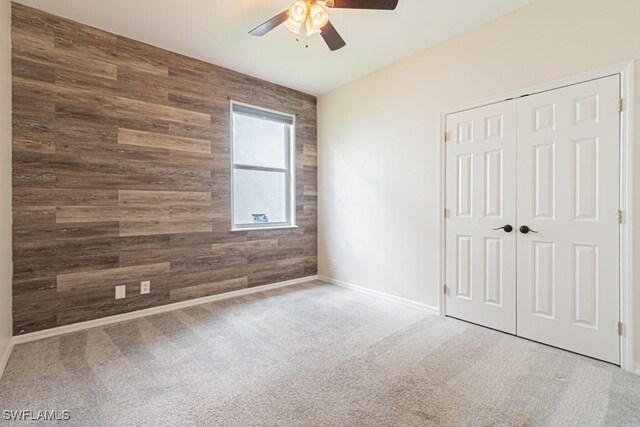 carpeted empty room featuring wood walls and ceiling fan