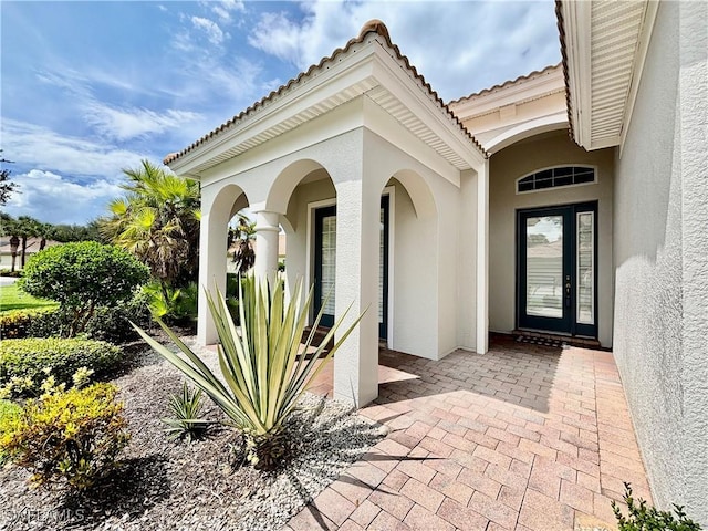 view of exterior entry with french doors, a tiled roof, and stucco siding