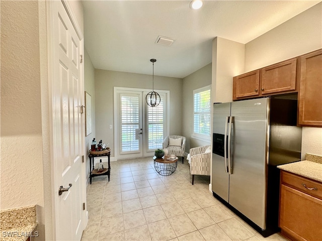 kitchen featuring french doors, light tile patterned flooring, decorative light fixtures, stainless steel fridge with ice dispenser, and light stone countertops