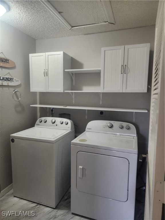 clothes washing area featuring washing machine and dryer, cabinets, a textured ceiling, and light wood-type flooring