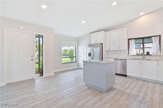 kitchen with a sink, tasteful backsplash, a center island, appliances with stainless steel finishes, and vaulted ceiling