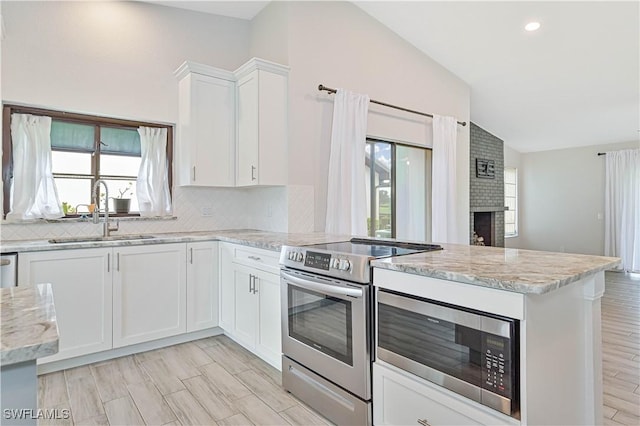 kitchen featuring a brick fireplace, vaulted ceiling, a peninsula, stainless steel appliances, and a sink