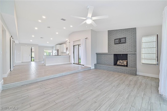 unfurnished living room with visible vents, lofted ceiling, light wood-style flooring, and a fireplace