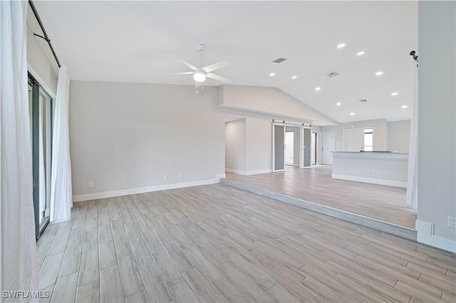 unfurnished living room featuring visible vents, lofted ceiling, ceiling fan, a barn door, and light wood-type flooring