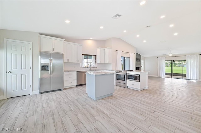 kitchen with appliances with stainless steel finishes, lofted ceiling, white cabinets, a center island, and ceiling fan