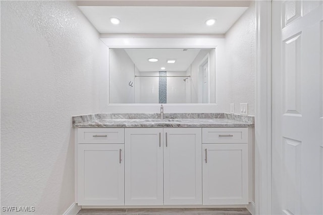 full bath with vanity, a shower stall, and a textured wall