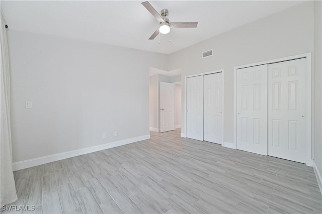 unfurnished bedroom featuring visible vents, light wood-style flooring, two closets, and baseboards