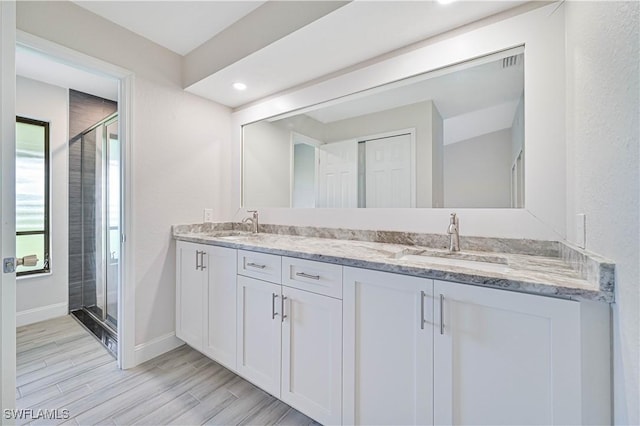 full bath featuring baseboards, wood finish floors, double vanity, a sink, and a shower stall