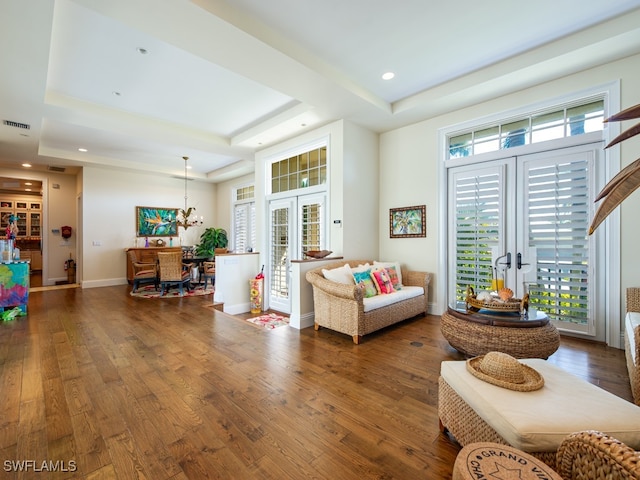 living room featuring a chandelier, a raised ceiling, dark wood-type flooring, and french doors