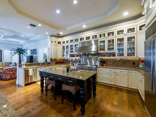 kitchen with kitchen peninsula, a kitchen island with sink, exhaust hood, and appliances with stainless steel finishes