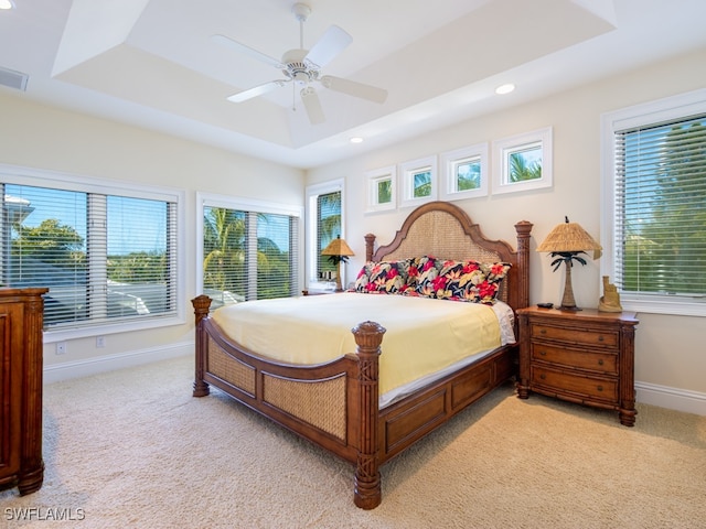 bedroom with a raised ceiling, multiple windows, ceiling fan, and light carpet