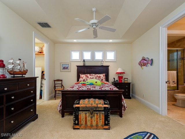 bedroom with ensuite bath, ceiling fan, a tray ceiling, a walk in closet, and light carpet