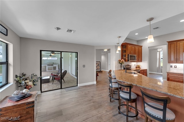 kitchen featuring hanging light fixtures, light wood-type flooring, stainless steel appliances, ceiling fan, and a breakfast bar area