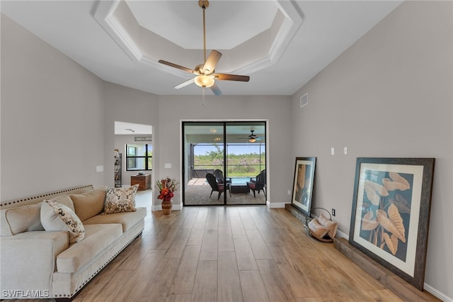 living room featuring a tray ceiling, ceiling fan, and light hardwood / wood-style flooring